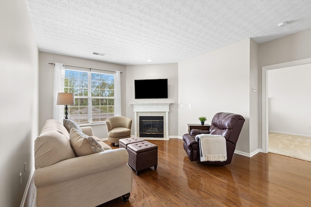 living room with baseboards, a textured ceiling, a tiled fireplace, and wood finished floors