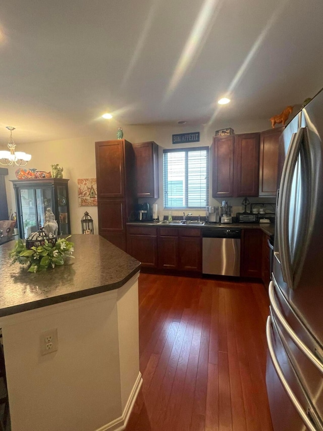 kitchen featuring dark countertops, a sink, a notable chandelier, stainless steel appliances, and dark wood-type flooring