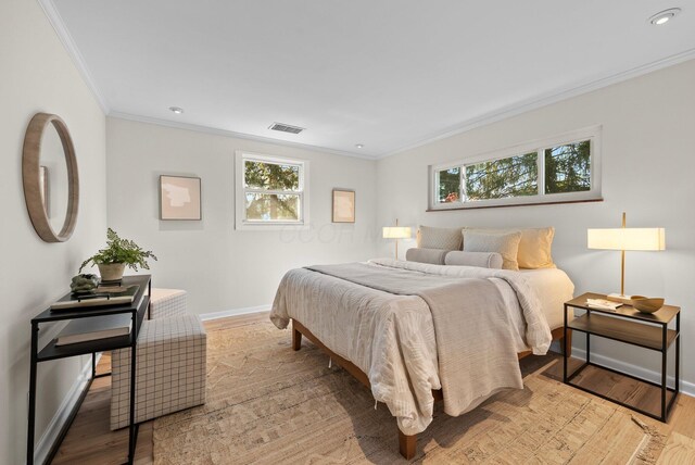bedroom with baseboards, visible vents, ornamental molding, and light wood-style flooring