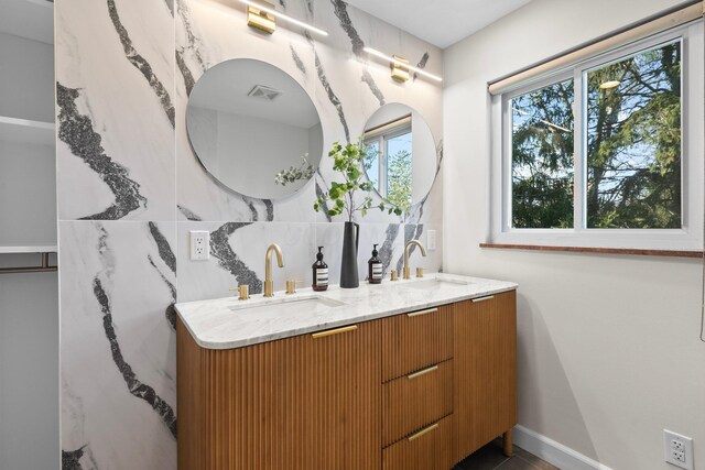 full bath featuring double vanity, a sink, baseboards, and visible vents