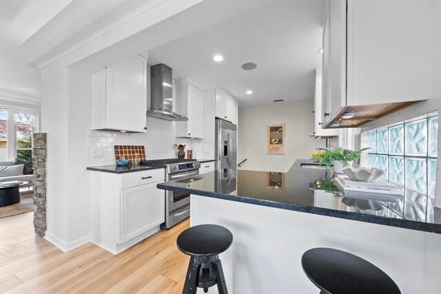 kitchen featuring light wood finished floors, wall chimney range hood, white cabinets, and stainless steel appliances