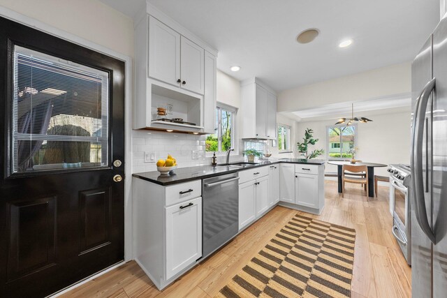 kitchen featuring appliances with stainless steel finishes, white cabinets, dark countertops, light wood finished floors, and a peninsula