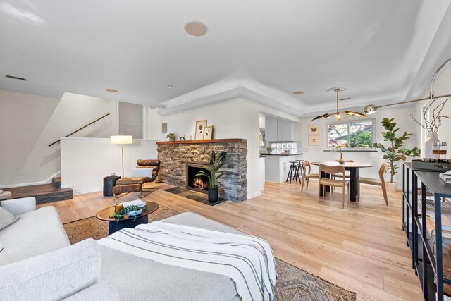 living area with light wood-style floors, visible vents, a stone fireplace, and stairway