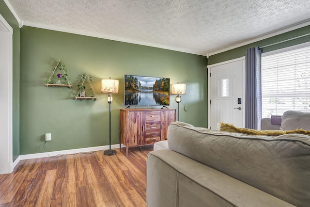living area with baseboards, ornamental molding, a textured ceiling, and wood finished floors