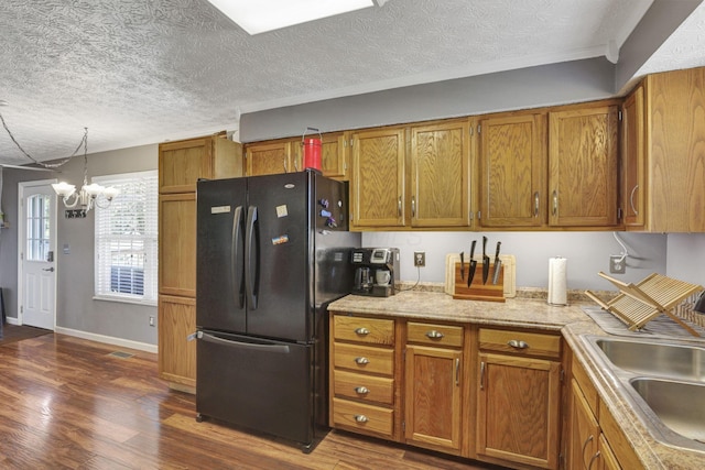 kitchen featuring brown cabinetry, a sink, freestanding refrigerator, an inviting chandelier, and dark wood-type flooring