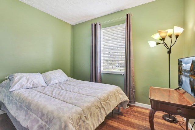 bedroom featuring baseboards, a textured ceiling, and wood finished floors