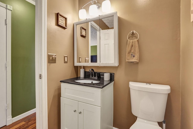 bathroom featuring vanity, baseboards, wood finished floors, and toilet