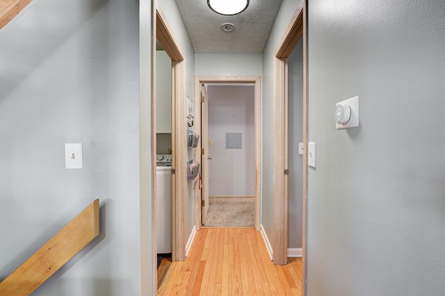 corridor featuring baseboards, light wood-style floors, and a textured ceiling