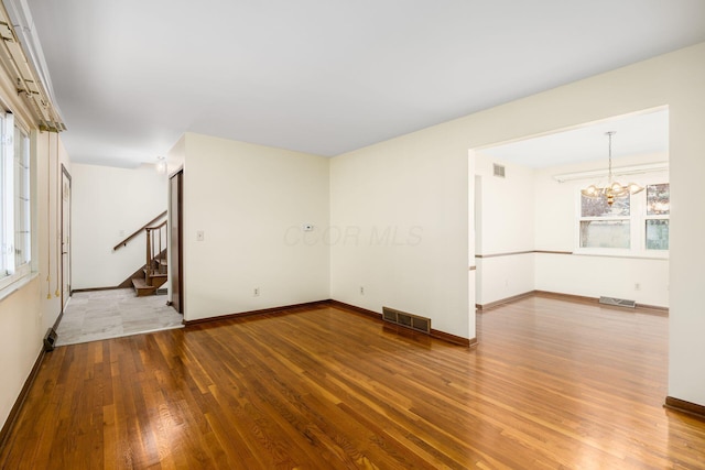 unfurnished living room with wood finished floors, visible vents, a chandelier, and stairs