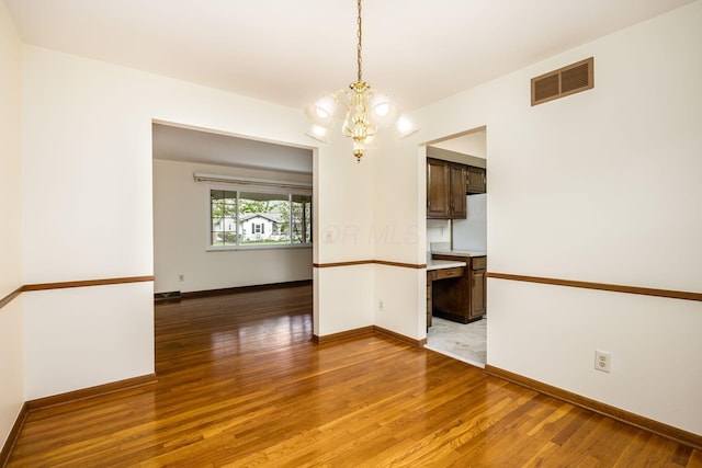 spare room with light wood finished floors, an inviting chandelier, visible vents, and baseboards