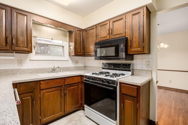 kitchen featuring gas stove, tasteful backsplash, light countertops, a sink, and black microwave