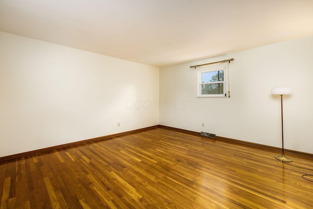 empty room featuring visible vents, wood finished floors, and baseboards