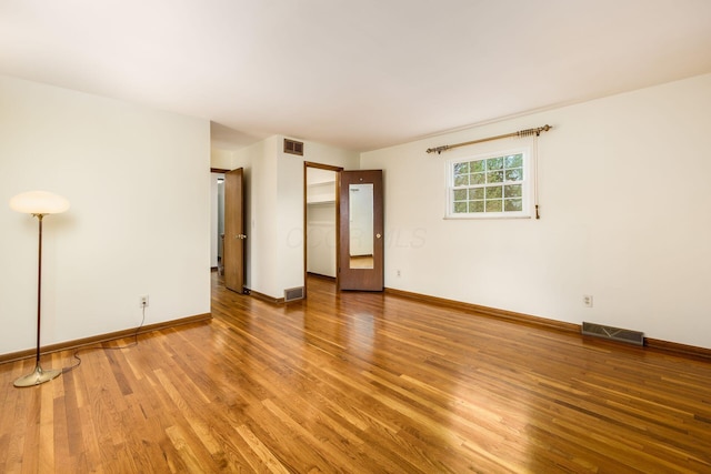 empty room with wood finished floors, visible vents, and baseboards