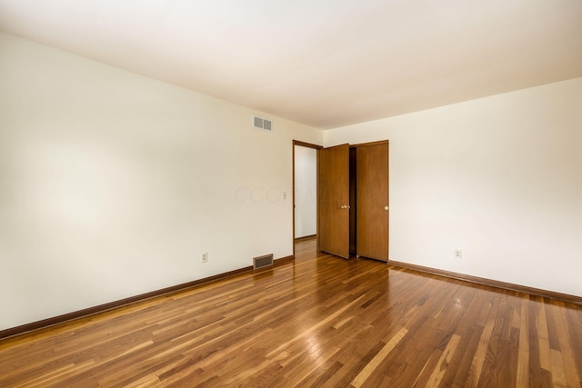 unfurnished room featuring wood finished floors, visible vents, and baseboards