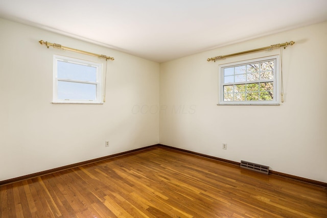 empty room with baseboards, visible vents, and wood finished floors
