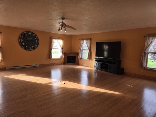 unfurnished living room with a textured ceiling, ceiling fan, baseboard heating, a fireplace, and a wealth of natural light