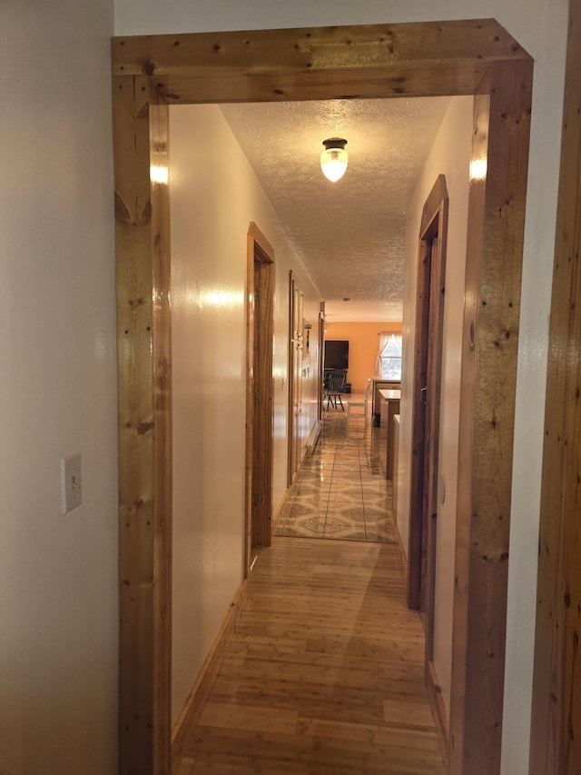 hall featuring a textured ceiling, light wood finished floors, and baseboards