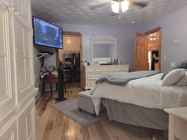 bedroom featuring light wood-style flooring, ceiling fan, freestanding refrigerator, a closet, and a spacious closet