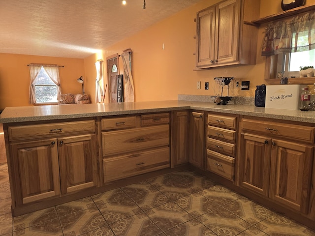 kitchen with dark tile patterned floors, a peninsula, a textured ceiling, and light stone counters