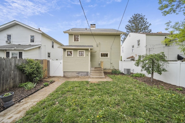 back of house featuring a fenced backyard, a chimney, a gate, central air condition unit, and a yard