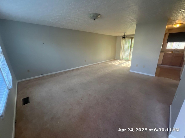 carpeted spare room featuring baseboards, visible vents, a wealth of natural light, and a chandelier
