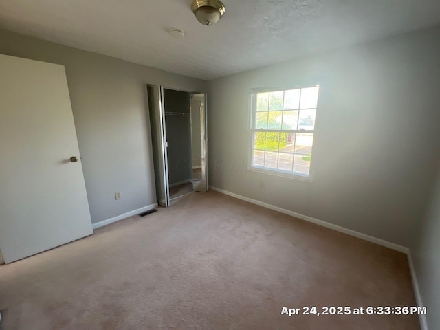 unfurnished bedroom with baseboards, visible vents, a closet, and light colored carpet
