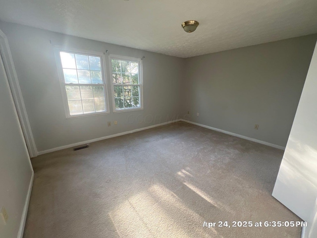 empty room featuring baseboards, visible vents, a textured ceiling, and carpet flooring