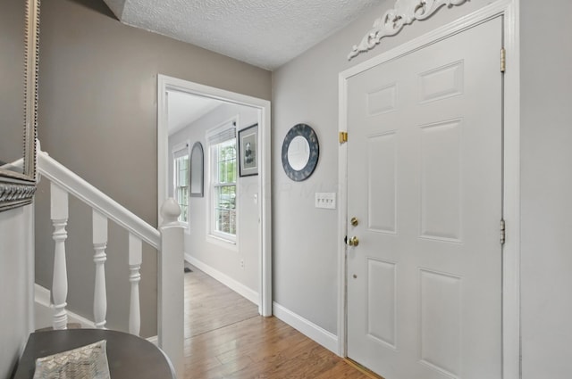 entrance foyer featuring a textured ceiling, stairs, wood finished floors, and baseboards
