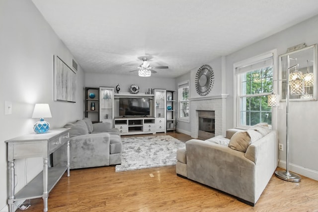 living room featuring a fireplace, a ceiling fan, visible vents, baseboards, and wood finished floors