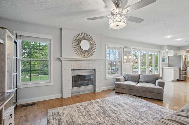 living area with baseboards, a ceiling fan, a textured ceiling, and a fireplace