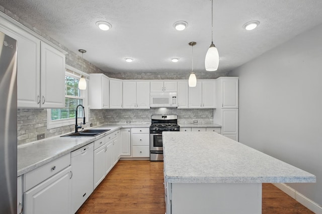 kitchen with wood finished floors, appliances with stainless steel finishes, backsplash, a sink, and a center island