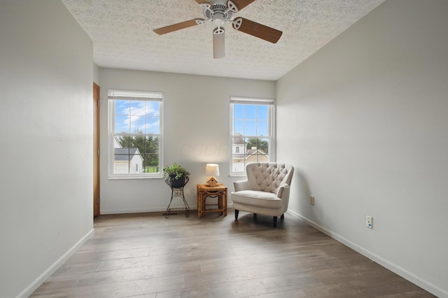 living area with a textured ceiling, wood finished floors, a ceiling fan, and baseboards