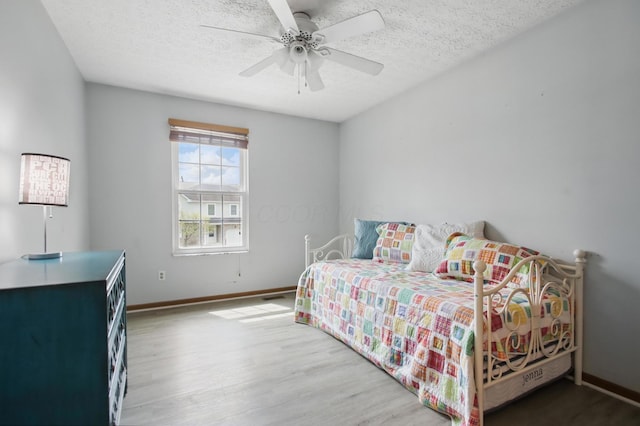 bedroom featuring a textured ceiling, visible vents, baseboards, wood finished floors, and a ceiling fan