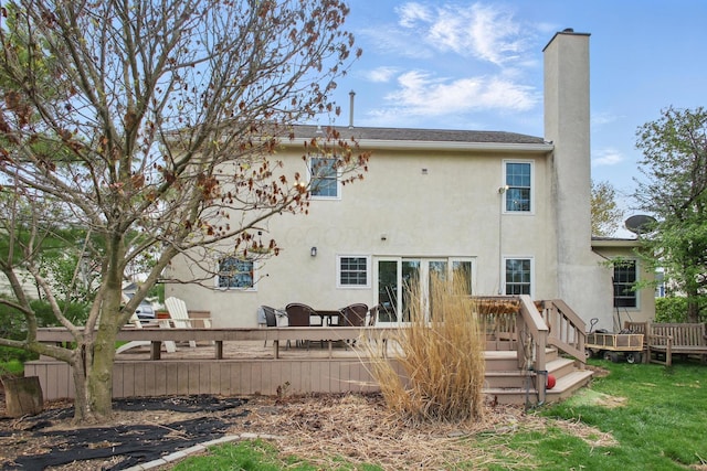 rear view of house with stucco siding, a chimney, and a wooden deck