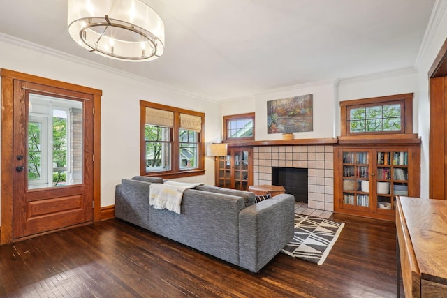 living room featuring dark wood finished floors, healthy amount of natural light, ornamental molding, and a tile fireplace