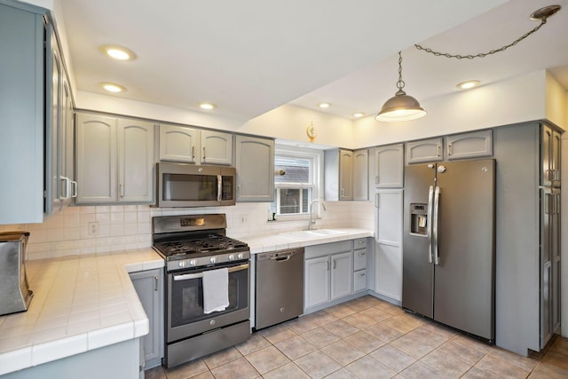 kitchen with appliances with stainless steel finishes, tile countertops, a sink, backsplash, and recessed lighting
