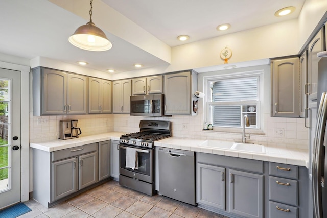 kitchen with appliances with stainless steel finishes, a sink, gray cabinets, tasteful backsplash, and light tile patterned floors
