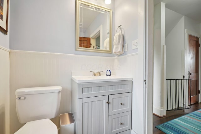 bathroom featuring a wainscoted wall, toilet, vanity, and wood finished floors