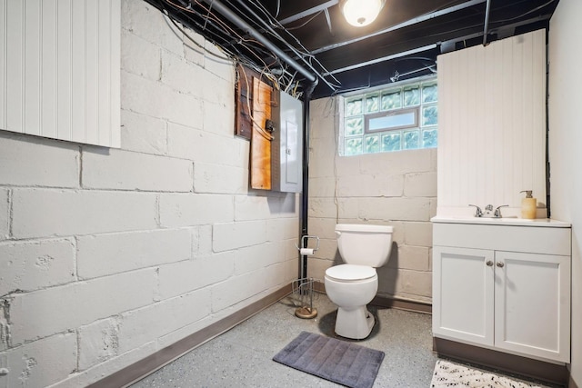 bathroom featuring toilet, vanity, electric panel, and concrete block wall