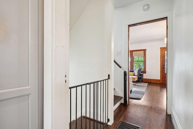 hallway featuring dark wood-type flooring, baseboards, an upstairs landing, and ornamental molding
