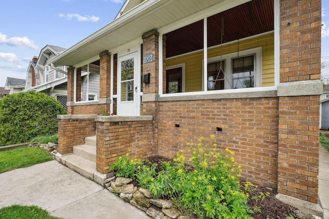 view of exterior entry featuring covered porch and brick siding