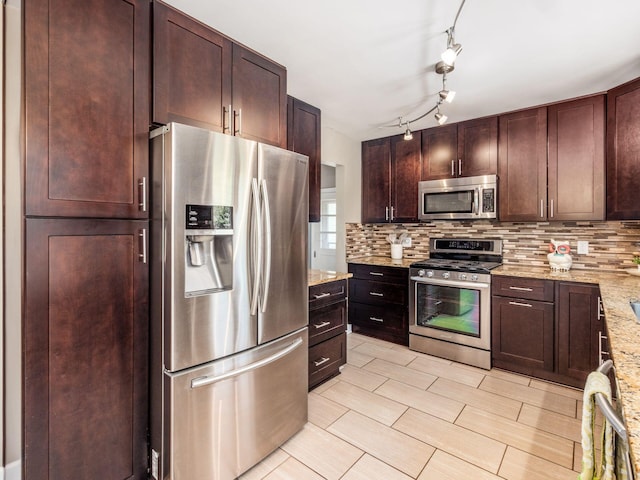 kitchen featuring dark brown cabinetry, light stone countertops, tasteful backsplash, rail lighting, and stainless steel appliances