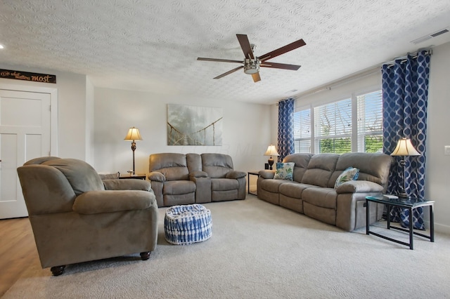 living room featuring visible vents, carpet flooring, a textured ceiling, and a ceiling fan