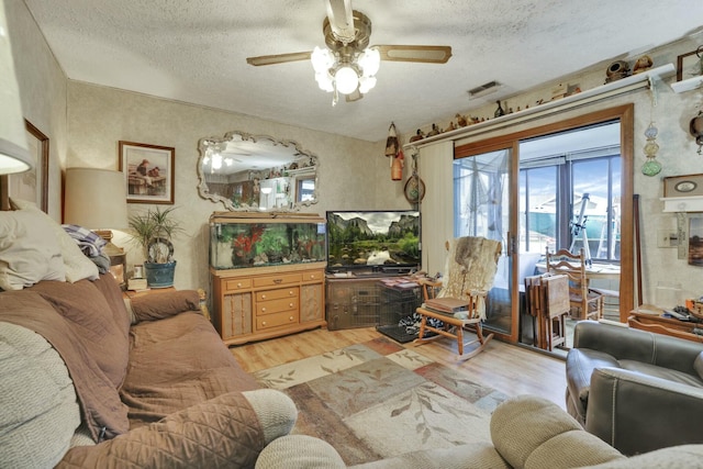living area featuring visible vents, ceiling fan, a textured ceiling, and light wood finished floors
