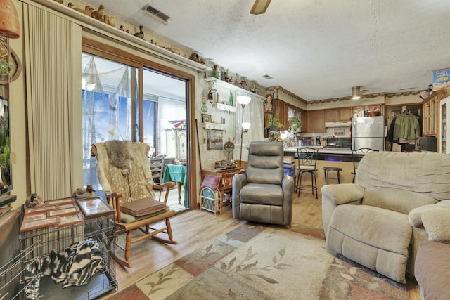 living room with visible vents, light wood-type flooring, ceiling fan, and a textured ceiling