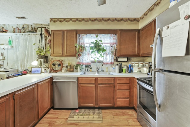 kitchen featuring a textured ceiling, a sink, appliances with stainless steel finishes, and light wood-style floors
