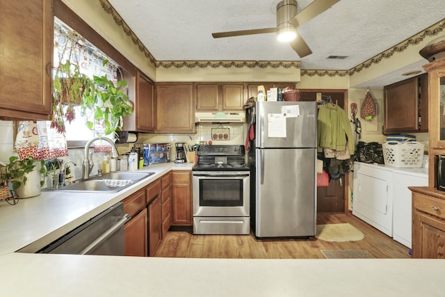 kitchen with under cabinet range hood, appliances with stainless steel finishes, light countertops, a sink, and a textured ceiling