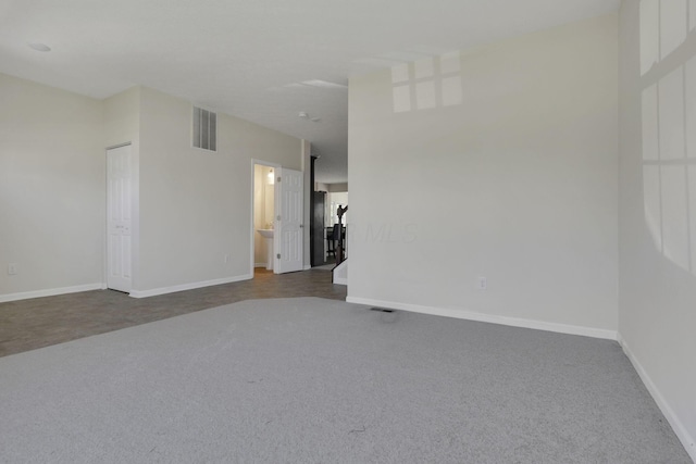 unfurnished room with baseboards, dark colored carpet, and visible vents