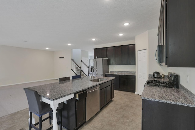 kitchen with a sink, dark stone counters, a kitchen island with sink, and stainless steel appliances