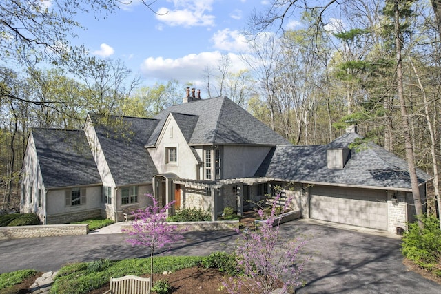 660 Woods Hollow Ln, Powell, OH 43065 - view of front of house featuring a chimney, stucco siding, driveway, stone siding, and an attached garage